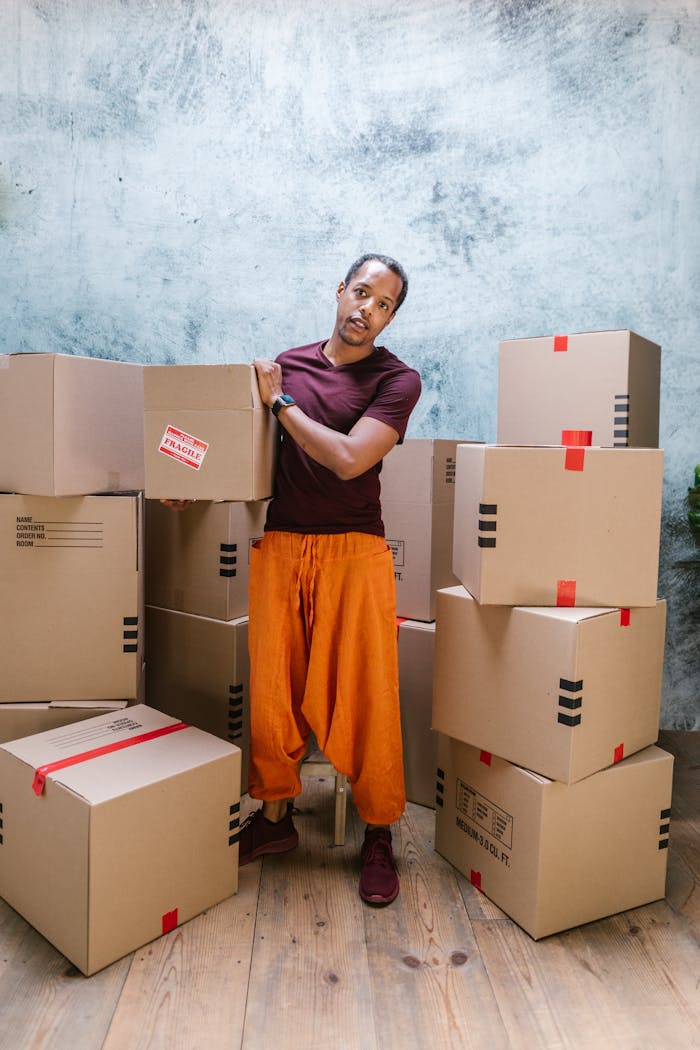 Man posing with cardboard boxes, symbolizing moving or delivery service indoors.